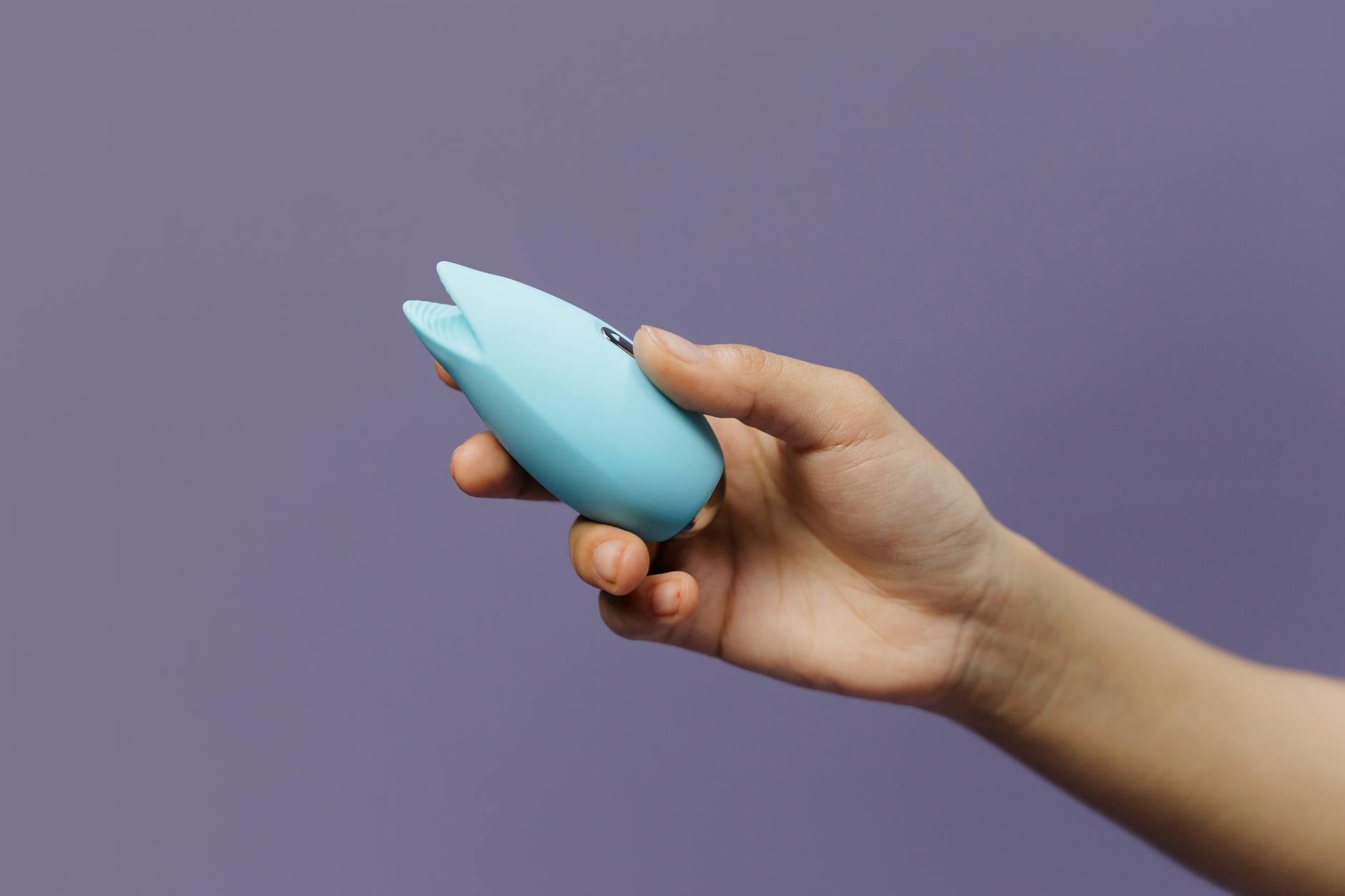 A blue silicone clitoral vibrator held in cupped hands against a solid background, symbolizing gentle sensation and self-care
