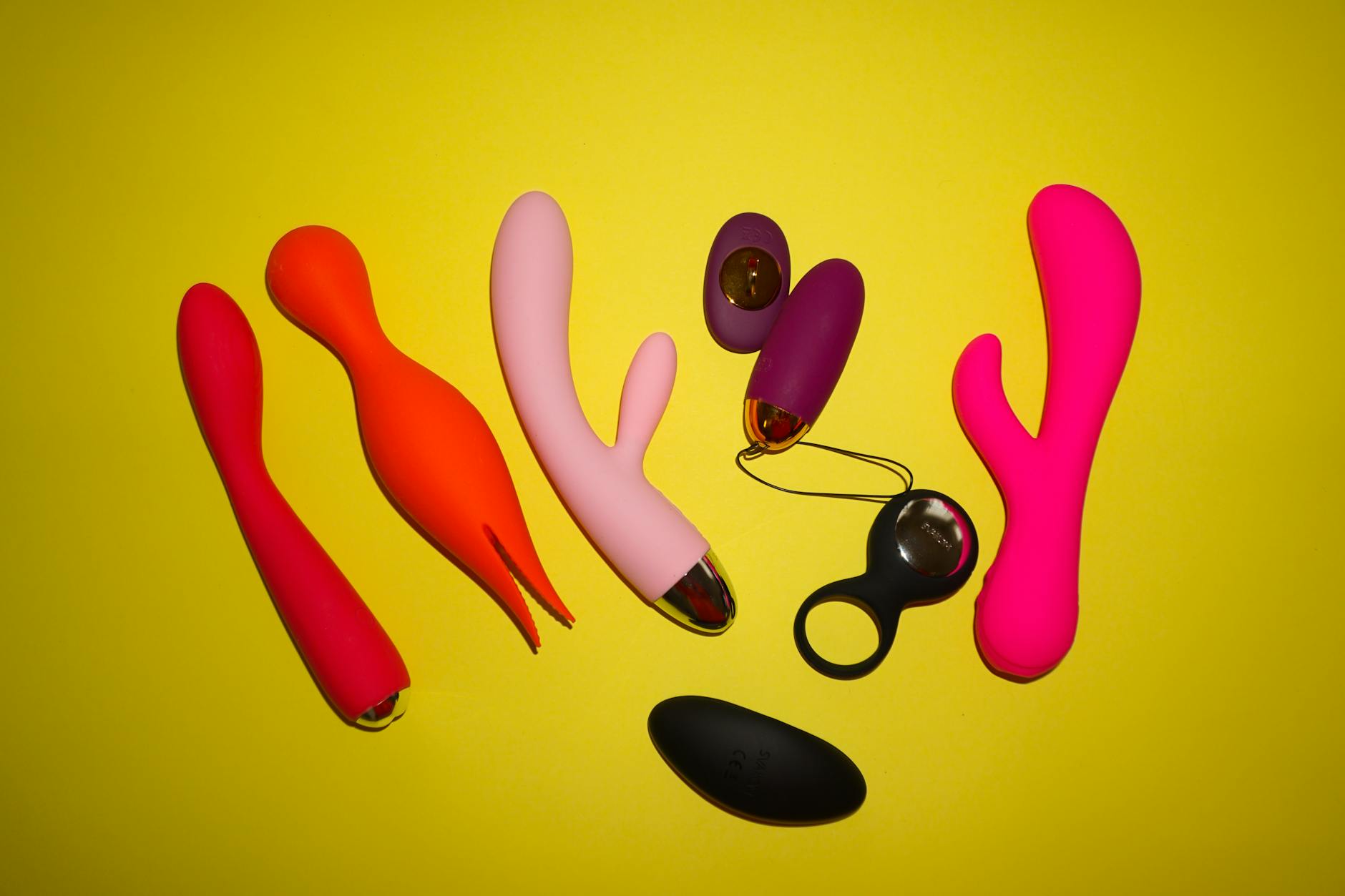 Two hands holding pink and blue silicone vibrators against a soft pastel background